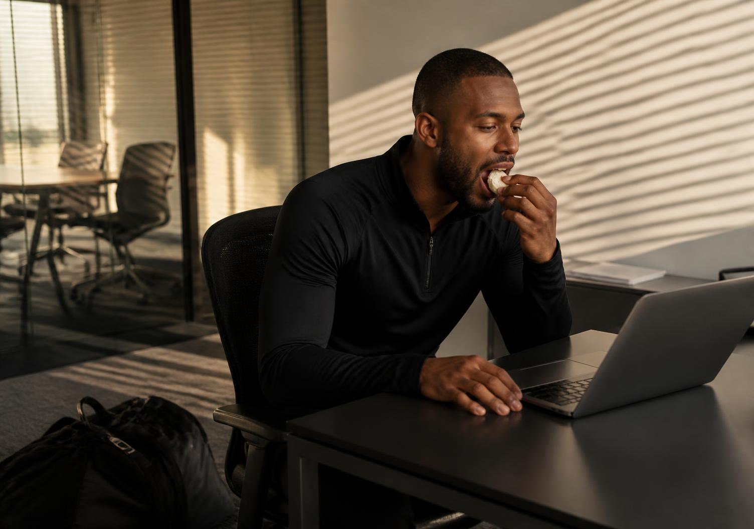 Professional eating a PUDD pillow at his desk with a gym bag beside him